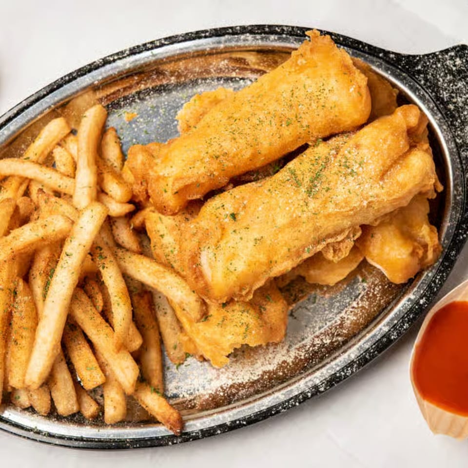 Golden-brown fish and chips, seasoned with herbs, served on a silver platter with a side of sauce.