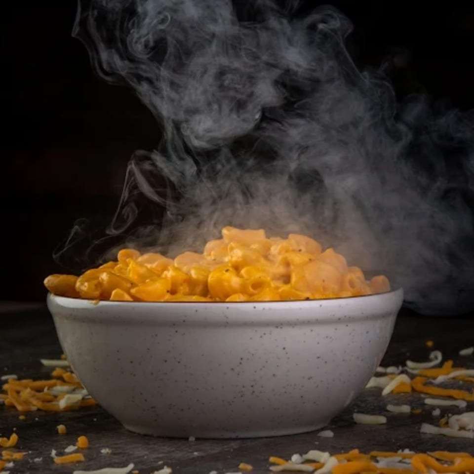 Steaming hot bowl of mac and cheese with shredded cheese scattered around it.