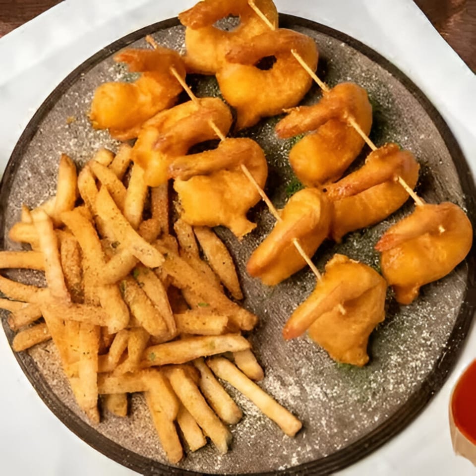 Times Square Kitchen's fried shrimp skewers and seasoned french fries on a dark round plate.