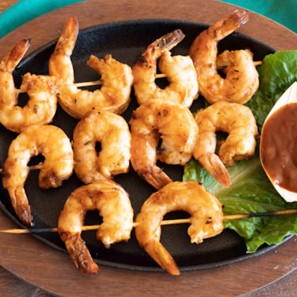 Grilled shrimp skewers with sauce on lettuce, served on a black plate at Times Square Kitchen.