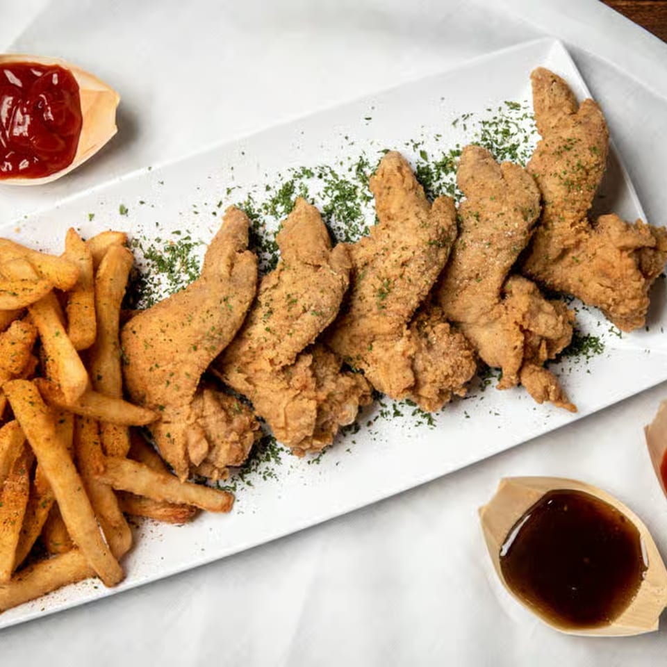 Crispy fried chicken tenders and golden french fries with ketchup and BBQ sauce on a white plate.