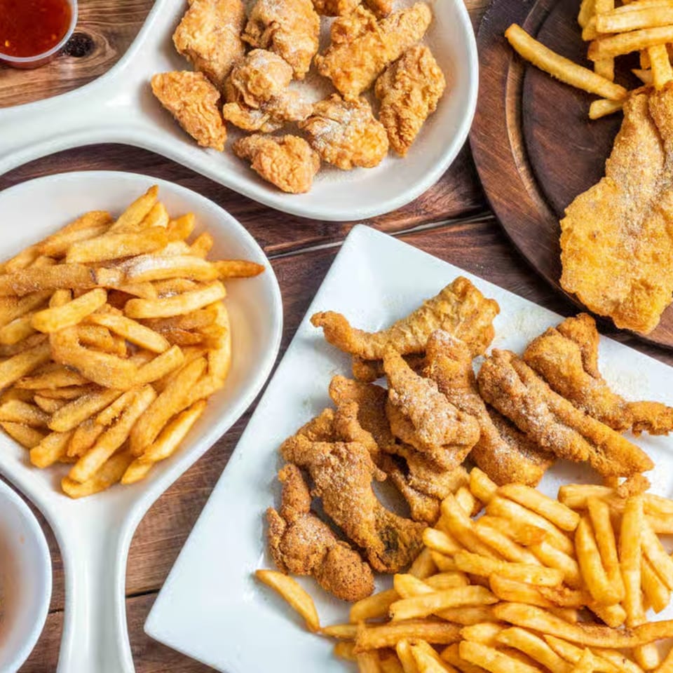 Plates of golden fried chicken tenders, fish, and french fries on a wooden table at Times Square Kitchen.